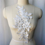Single white floral applique embroidered with metallic thread and embellished with sequinned leaves and 3D flowers that have a crystal centre.  The applique is displayed on a mannequin. 