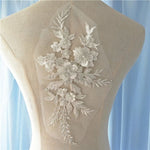 Heavily beaded white floral applique embroidered onto a net backing.  The applique is decorated with 3D fabric flowers that have a beaded centre.  The applique is displayed on a mannequin.