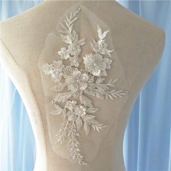 Heavily beaded white floral applique embroidered onto a net backing.  The applique is decorated with 3D fabric flowers that have a beaded centre.  The applique is displayed on a mannequin.