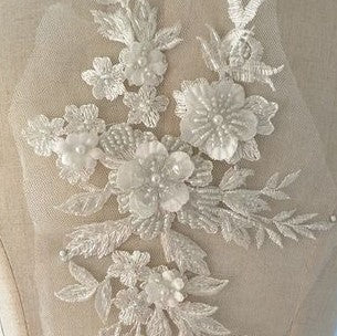 Close up view of beaded white floral applique.  The applique has larger and smaller  3D fabric flowers that have beaded centres.