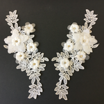 White lace floral applique pair decorated with 3D flowers that have a crystal centre.  The appliques are laying flat on a black background.