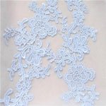 Close up view of pale blue embroidered applique pair laying flat on a white background.