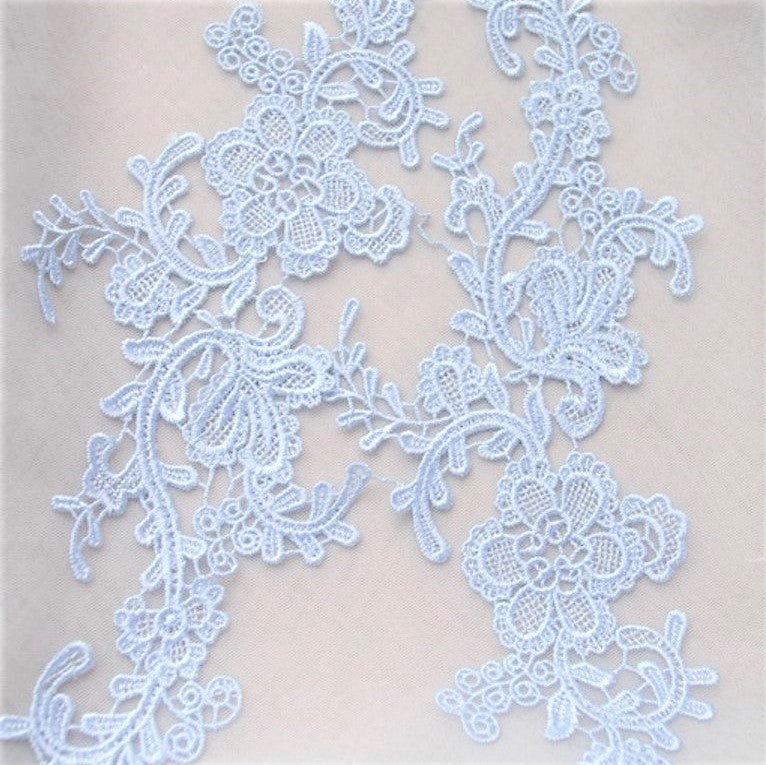Close up view of pale blue embroidered applique pair laying flat on a white background.