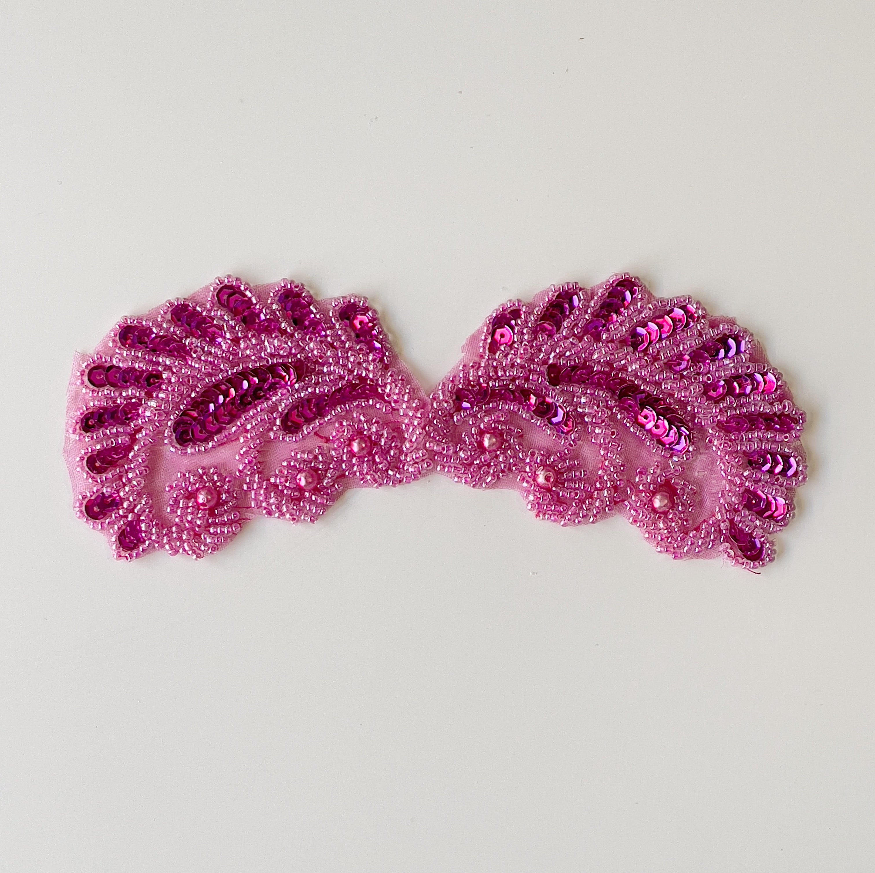 Fuchsia beaded shell shaped applique pair embellished with sequins laying flat on a white background.