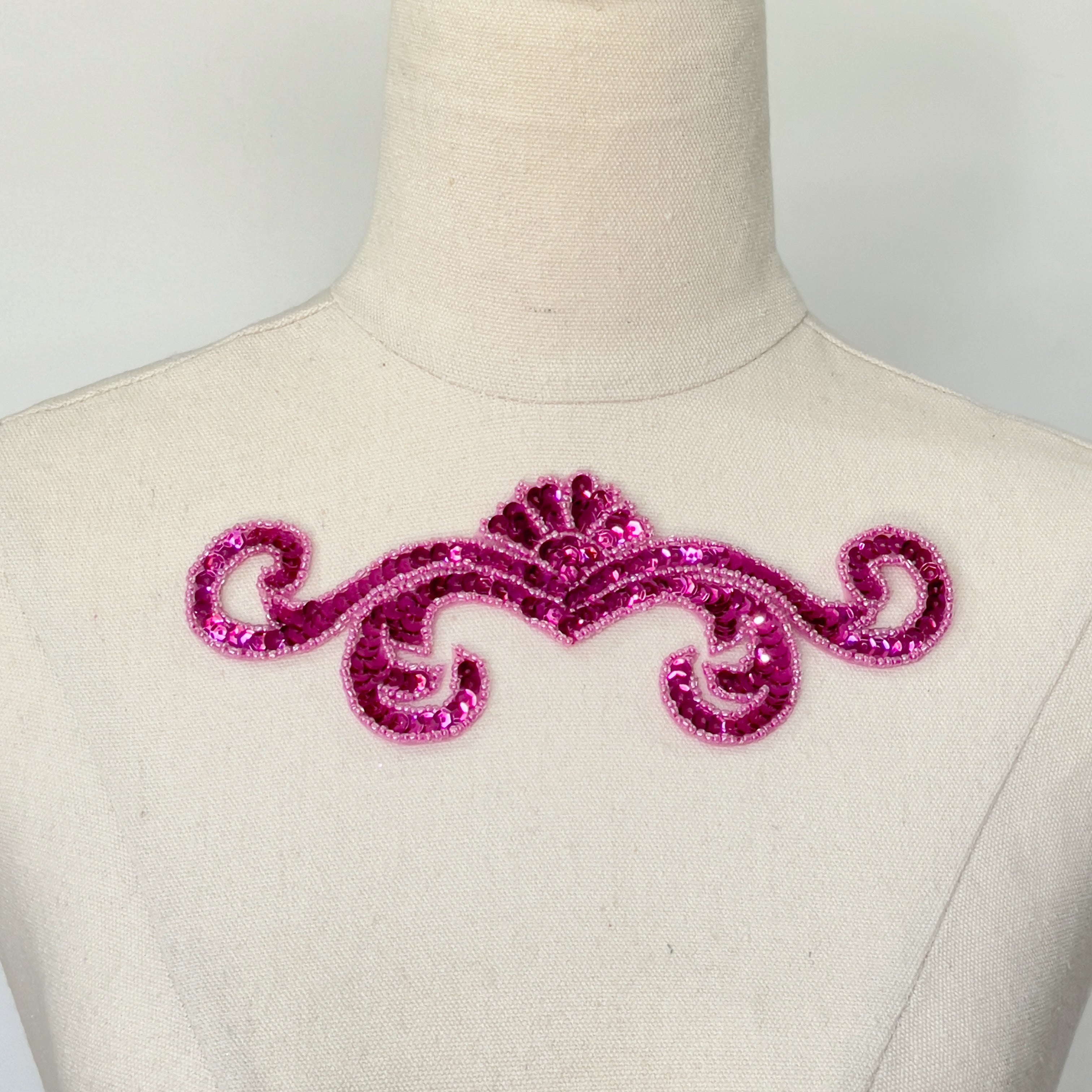 Single fuchsia sequin scroll bodice applique filed with fuchsia sequins and edged with fuchsia seed beads displayed on a mannequin.