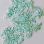 Close up image of embroidered and corded mint green lace applique with floral design.