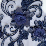 Close up view of navy blue floral applique embroidered onto a navy net backing.  The image shows two 3D flowers.