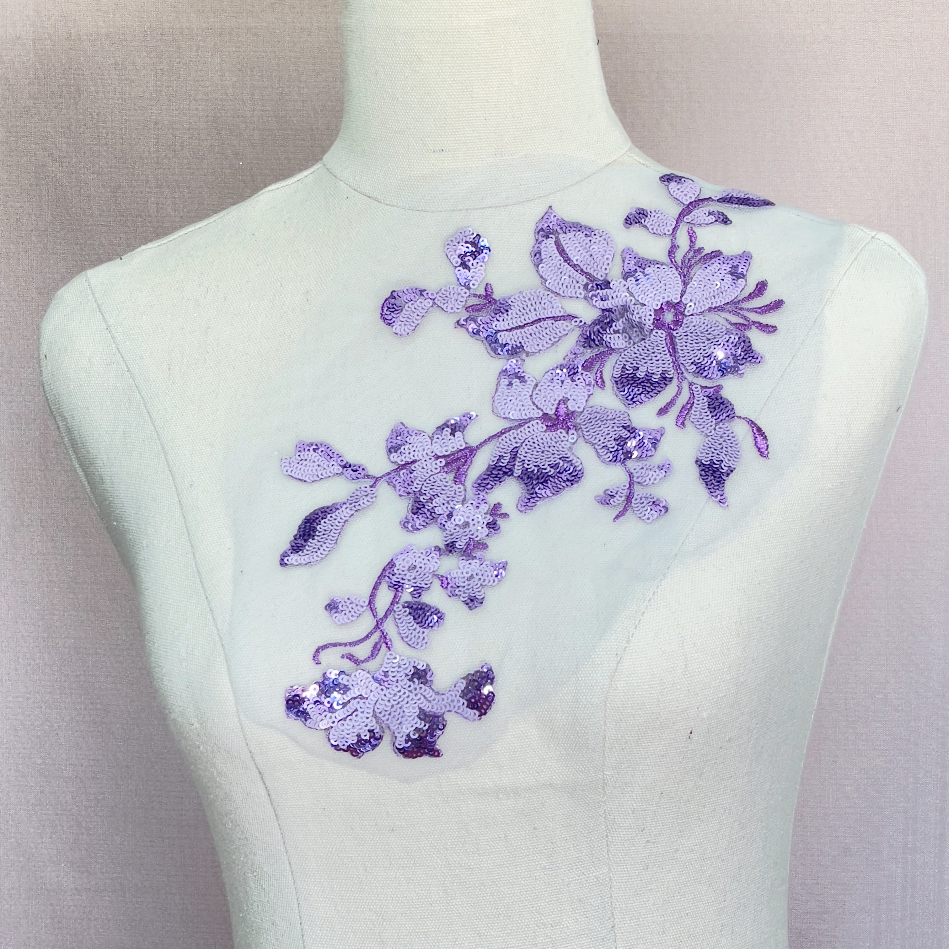Fully sequinned single floral applique in varying shades of light and mid purple on a white net backing.  The stems and leaves of the flowers are embroidered with metallic purple thread.   