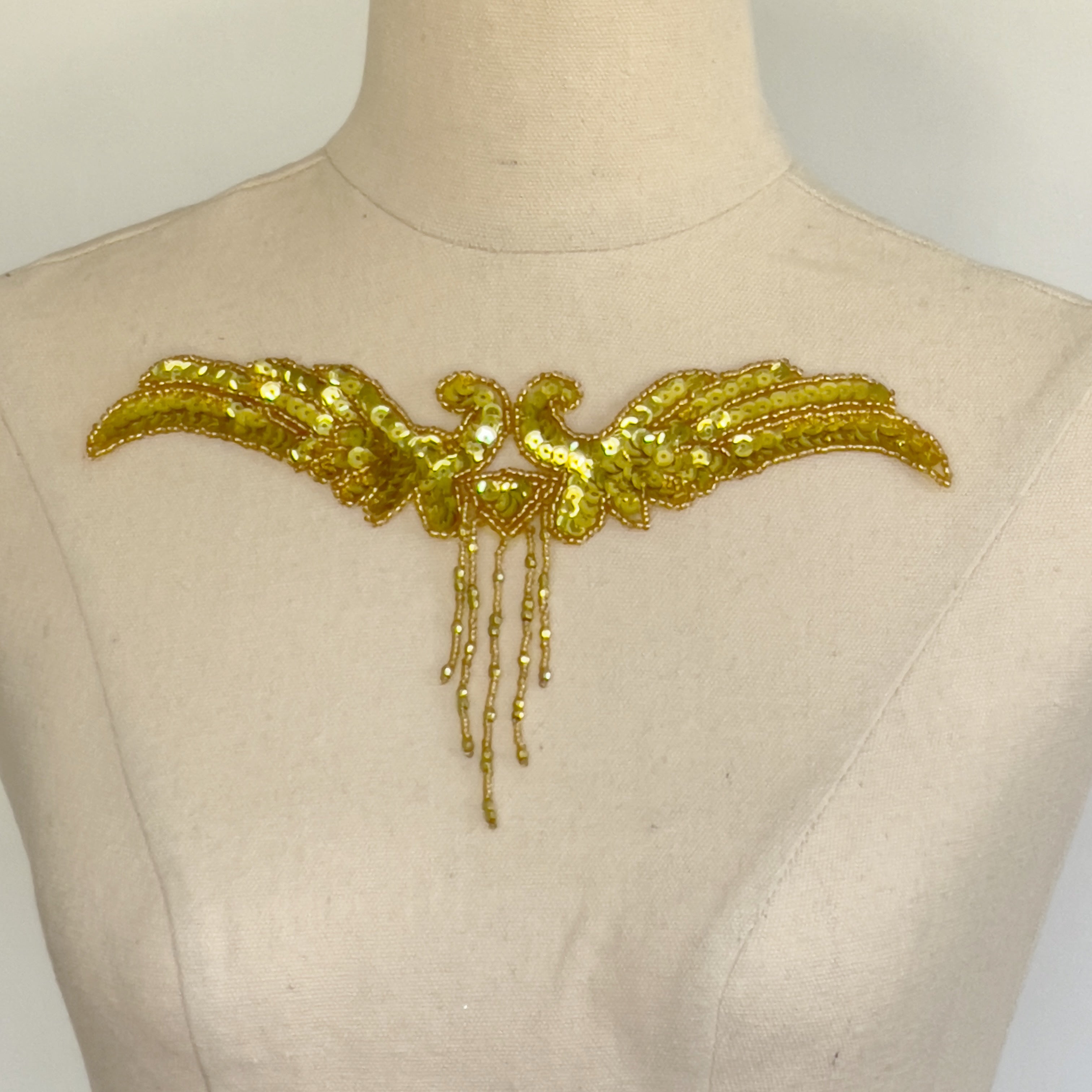 Gold sequinned bodice applique edged with gold seed beads.  The centre front has a five strand seed bead fringe.  The applique is displayed on a mannequin.    
