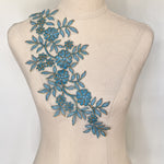 Blueembroidered applique with brassy gold cording outlining all the leaves stems and flowers . the applique is draped across a mannequin bodice e