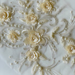 A closeup of a cream an ivory applique showing 3D flowers cream and silver embroidered  leaves  and pearl embellishments