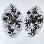 Black 3D floral applique pair decorated with beads and embroidered onto a net backing.  The appliques are laying flat on a white background. 