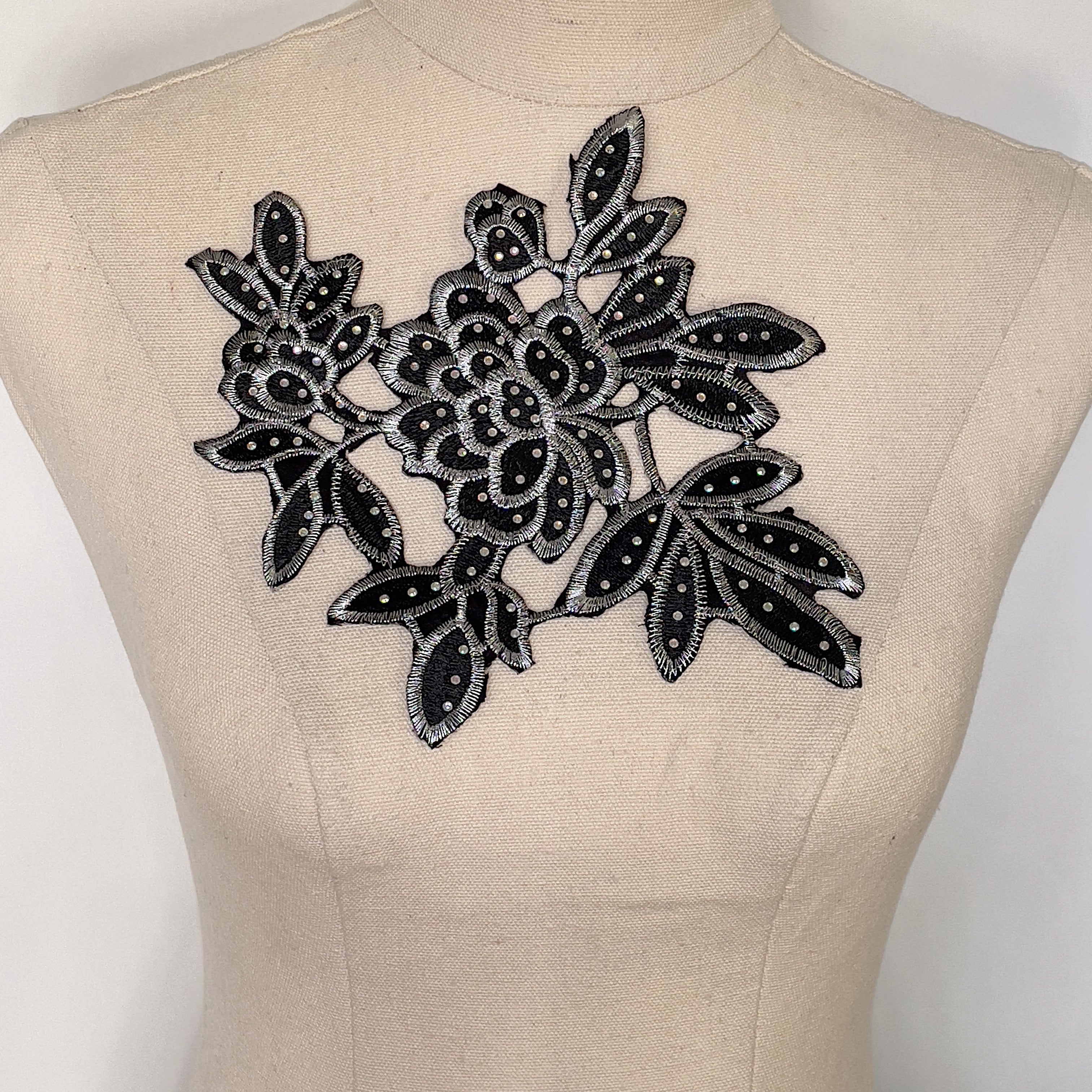 A silver and black applique with a large central flowers surrounded by clusters of leaves. 