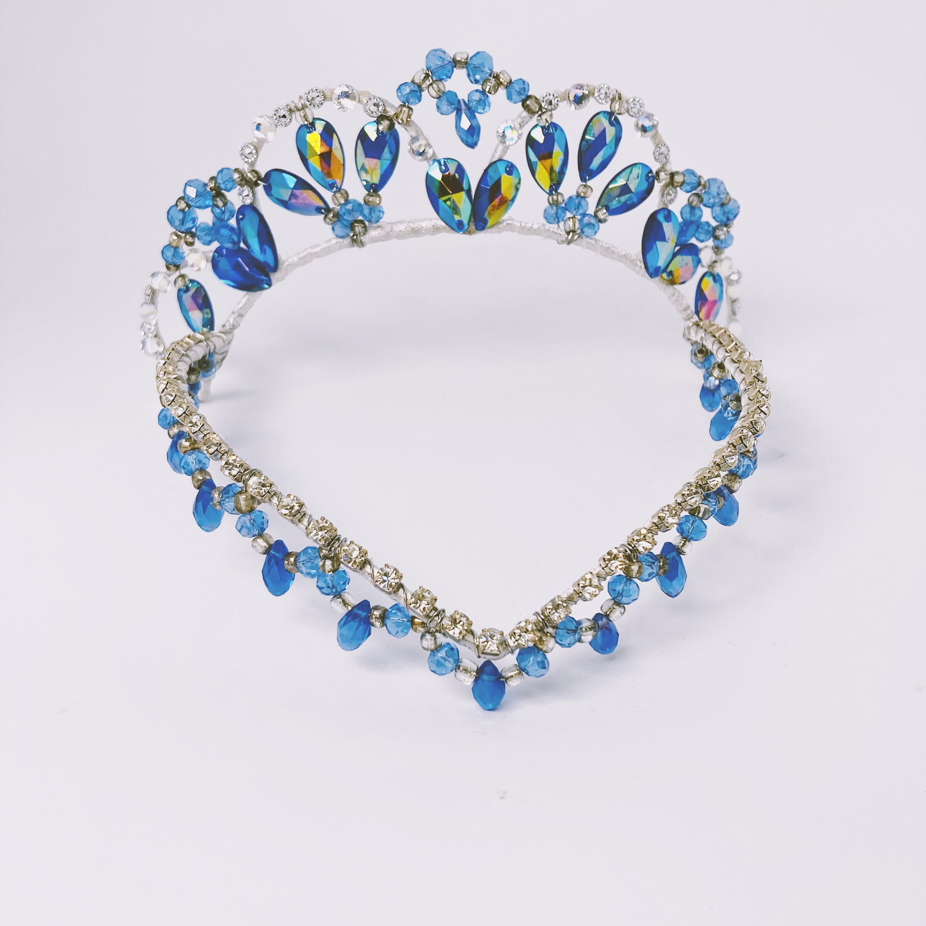 Front view of blue and silver tiara featuring blue AB crystals and a v shaped forehead piece embellished with rhinestones and fringed with blue drop beads. 