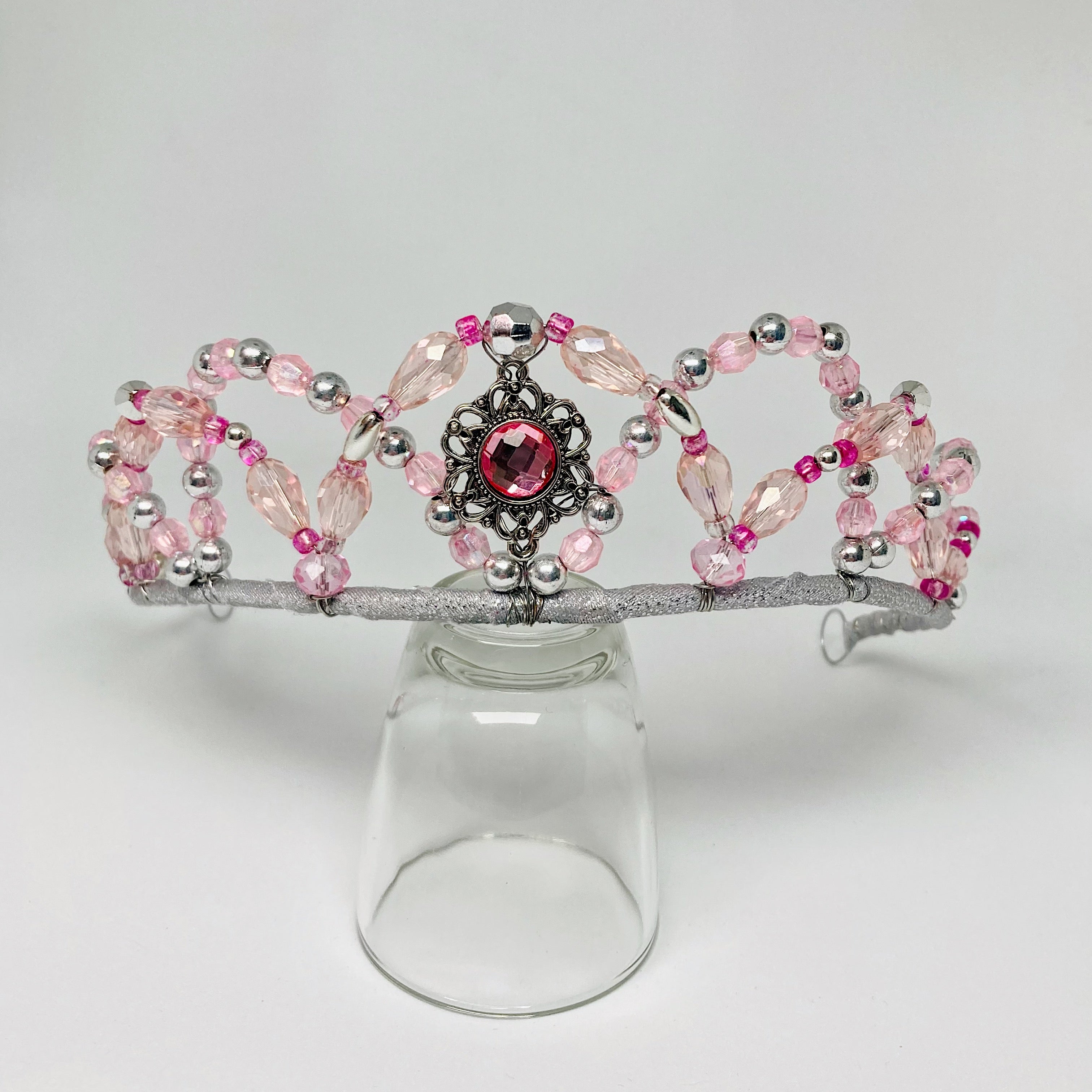 Front view of pink and silver beaded tiara with a central medallion displayed on a clear glass.