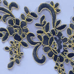 Close up view of a black embroidered applique edged with metallic gold cord.
