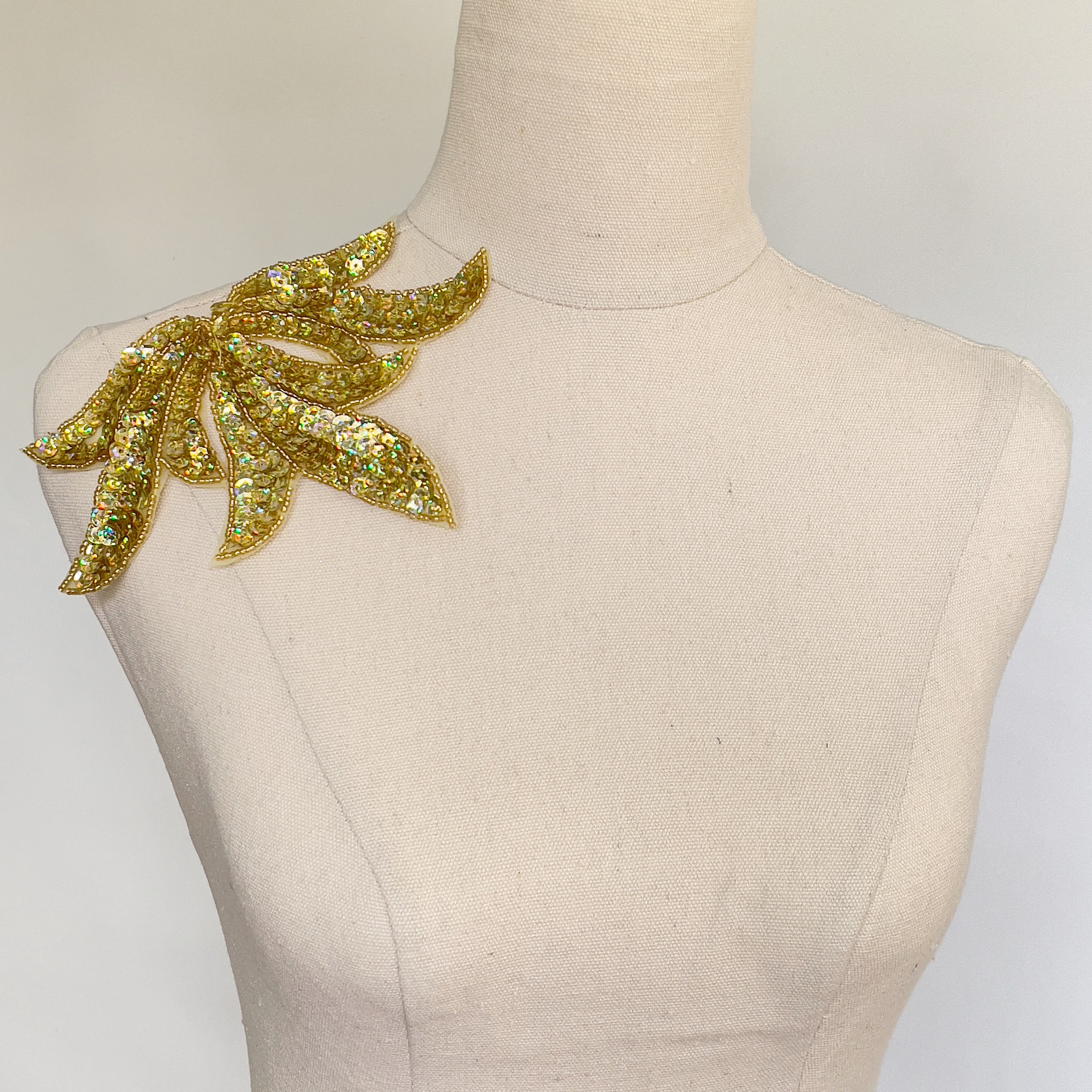 Leaf shaped applique filled with gold sequins and displayed on a mannequin.
