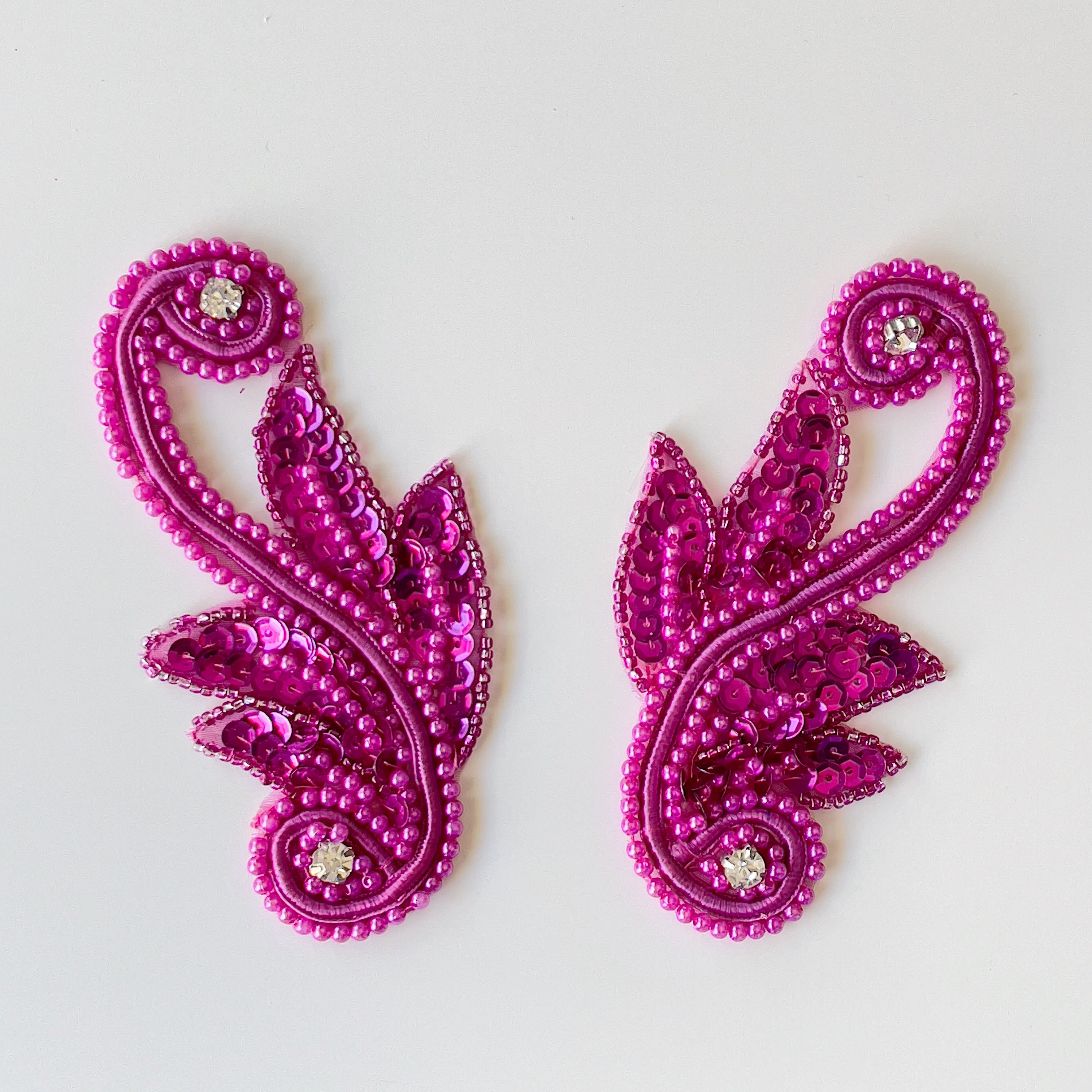 Fuchsia beaded scroll applique pair with embellished with sequins and crystal rhinestones laying flat on a white background.