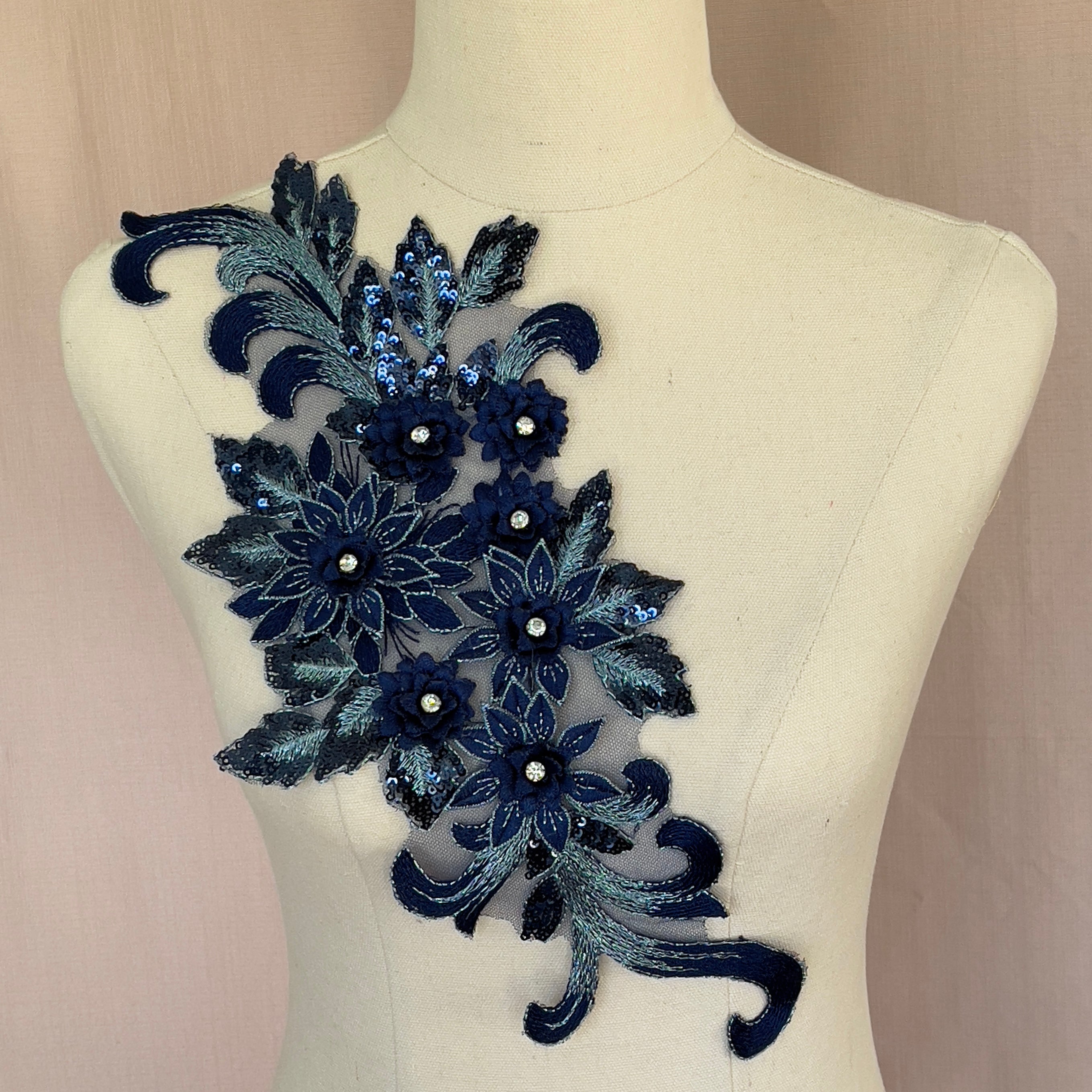 Single floral navy blue applique embroidered with silver metallic thread and embellished with small black sequins. The 3D flowers have crystal centres.  The applique is displayed on a mannequin.  