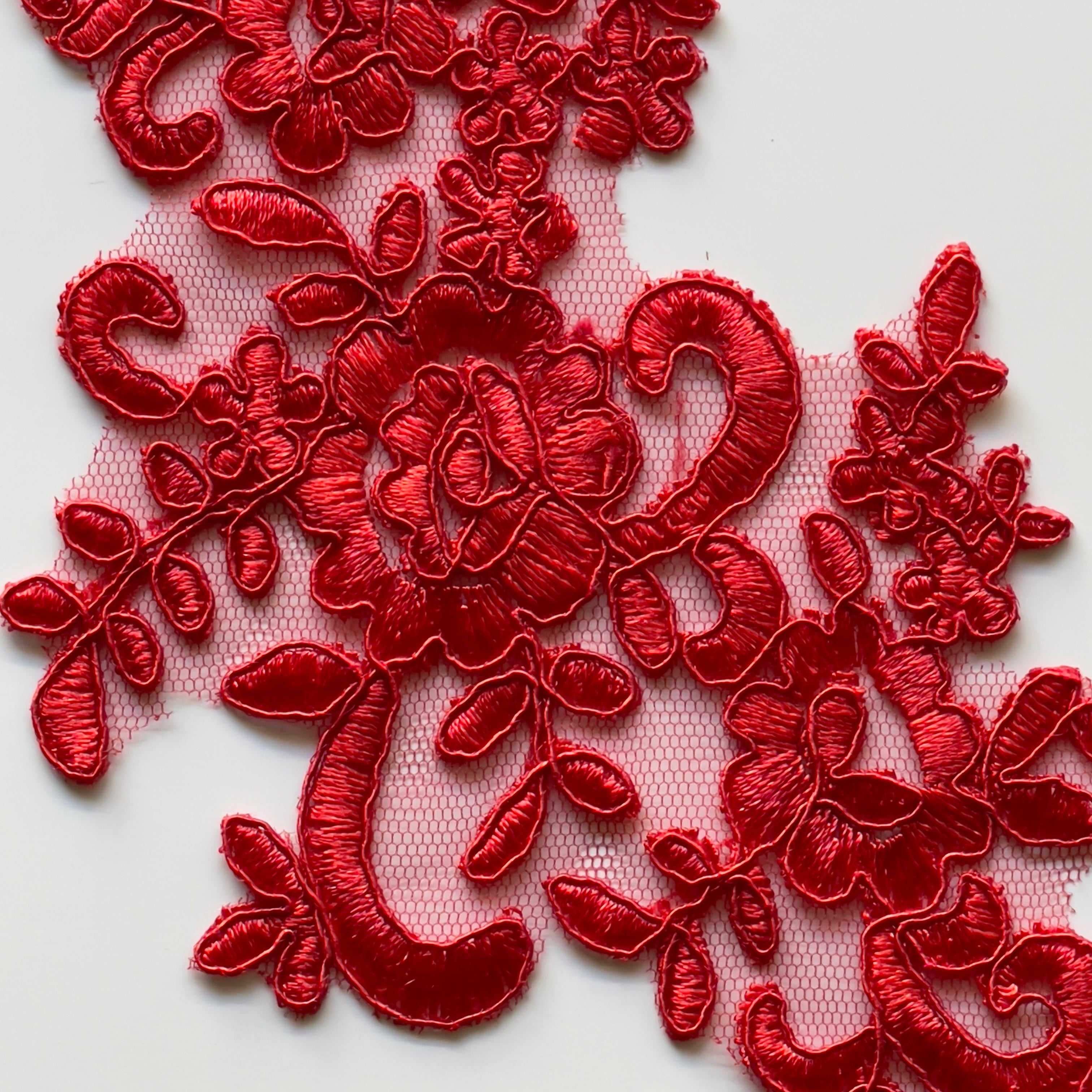 Close up of red floral applique embroidered onto a red net backing.  The applique is laying flat on a white background.