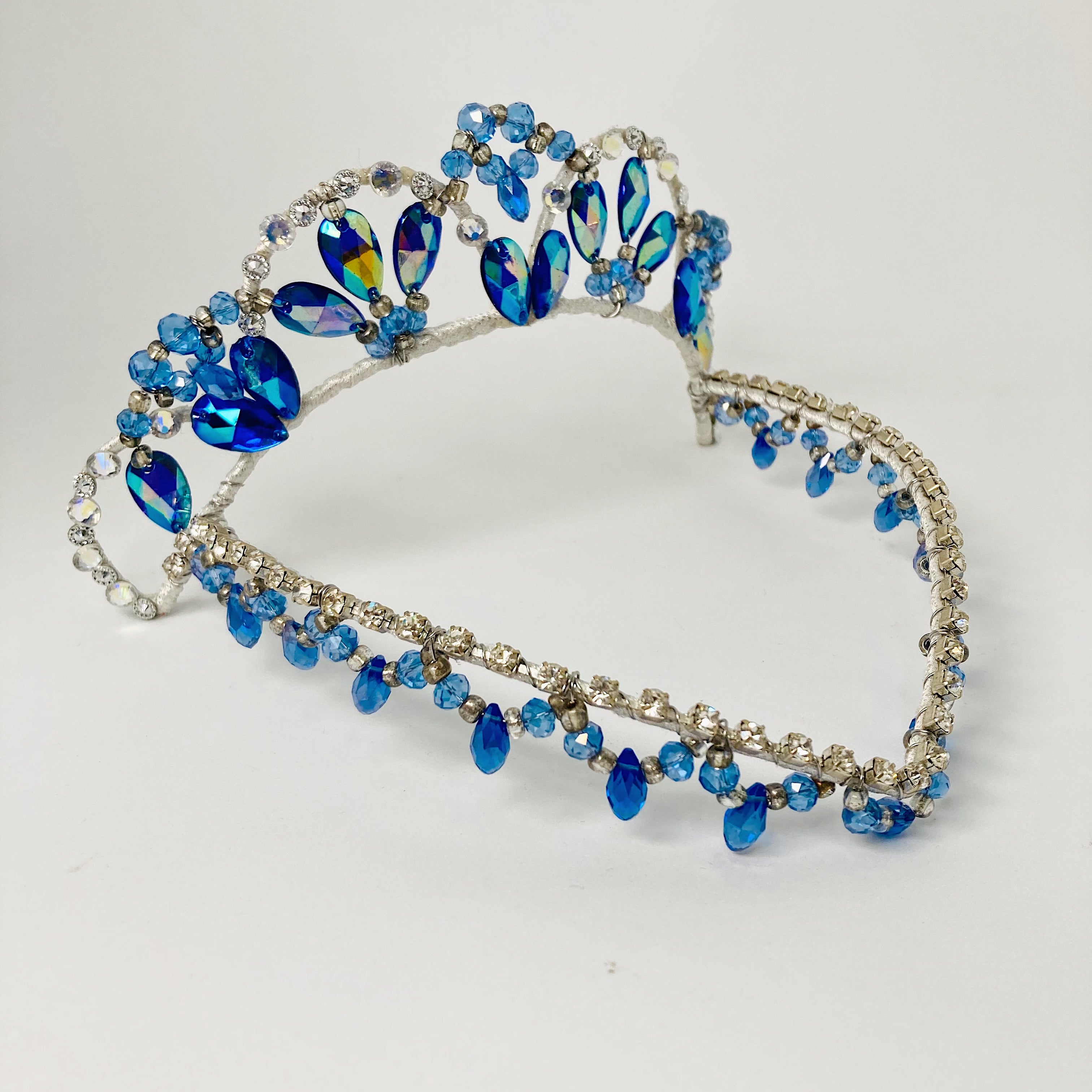 Front view of blue and silver tiara featuring blue AB crystals and a v shaped forehead piece embellished with rhinestones and fringed with blue drop beads. 